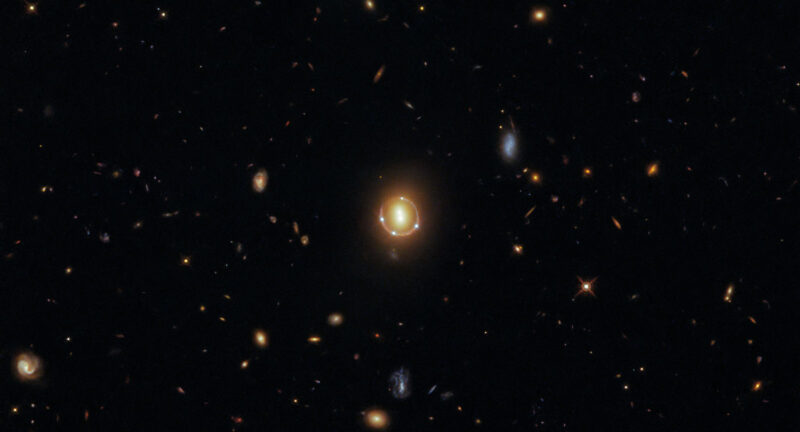 Quasar 2M1310-1714 es visible como cuatro puntos de luz alrededor de una luz central gracias a lentes gravitacionales.  Es una imagen del espacio superior.