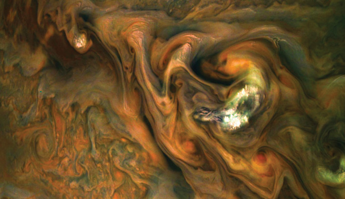 imagen de nubes anaranjadas, blancas, verdes y marrones girando en la atmósfera de Júpiter