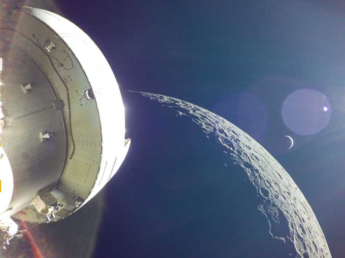 la nave espacial Orión en primer plano con la luna prominente en el fondo.  La Tierra está representada por una media luna delgada, así como por un destello de lente grande con un pequeño punto en el medio, que es el sol.