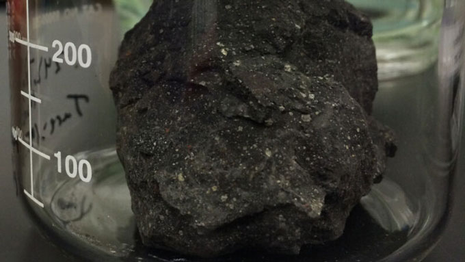 Una foto de una pieza de meteorito negro de dos gramos dentro de un vaso de precipitados